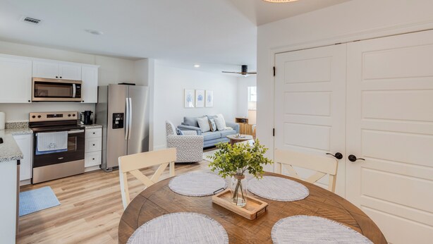 A modern kitchen with stainless steel appliances, a dining area with a wooden table and chairs, and a living room with a sofa and decorative pillows. - Coastal Charm! 2-bedroom house in lovely Gulfport. (Gulfport)