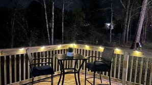 A wooden deck with a table and chairs, surrounded by a railing with string lights. - Coastal Charm! 2-bedroom house in lovely Gulfport. (Gulfport)