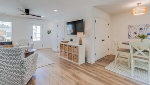 A spacious living area with a modern ceiling fan, a flat-screen TV mounted on the wall, a dining table with chairs, and a white cabinet with wicker baskets. - Coastal Charm! 2-bedroom house in lovely Gulfport. (Gulfport)