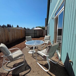 A patio area with a round table and four chairs, surrounded by a wooden fence. - Family-Friendly One-Level Home in Aloha (Beaverton)