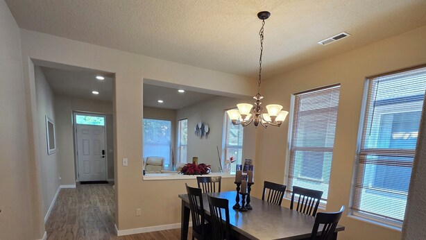 A dining area with a wooden table and chairs, a chandelier, and a view of the kitchen through an archway.