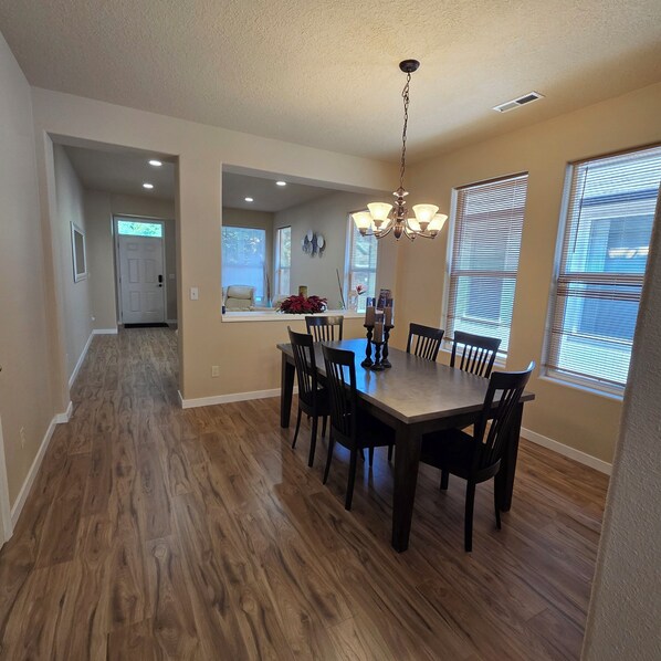 A dining area with a wooden table and chairs, a chandelier, and a view of the kitchen through an archway. - Family-Friendly One-Level Home in Aloha (Beaverton)