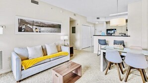 A modern living room with a sofa, coffee table, and dining area with chairs. - “Spacious 1BR Grand Suite | Full Kitchen, Balcony & Near Universal Parks” (Orlando)