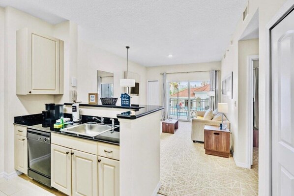 A modern kitchen with a dishwasher, stove, and sink. There is a dining area with a table and chairs. - “Spacious 1BR Grand Suite | Full Kitchen, Balcony & Near Universal Parks” (Orlando)