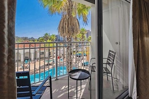 Balcón con vista a una piscina y zona de playa, incluyendo sillones de descanso y una mesa.