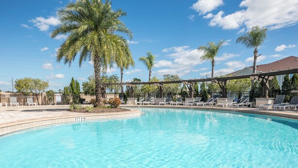 A clear blue pool with lounge chairs and palm trees. - Charming 3-bedroom house close to Disney in Kissimmee (Kissimmee)