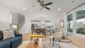 Uma sala de estar ampla, com sofá, poltronas, mesa de centro e, ao fundo, um espaço para refeições.