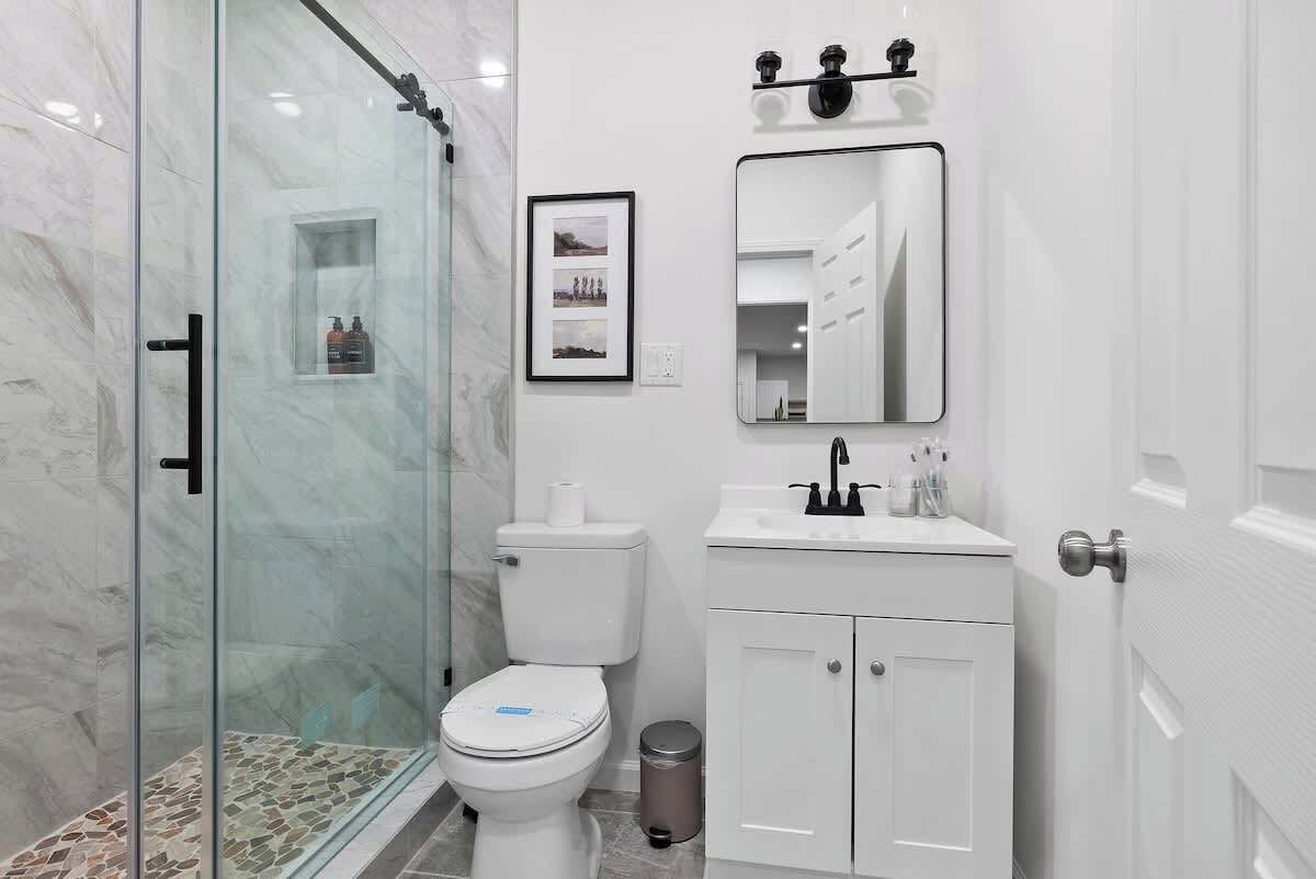 Et moderne badeværelse med et glasbrusekabine, toilet, vask med spejl over og et skab nedenunder.