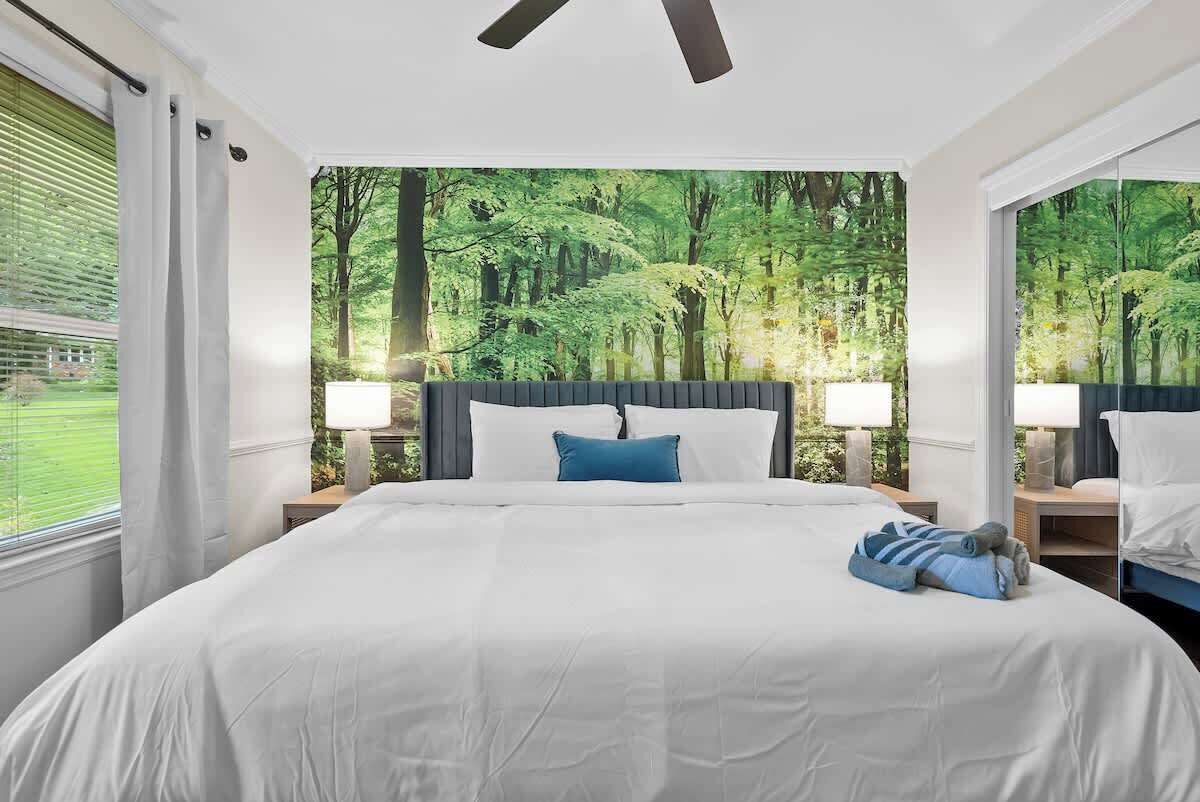 A hotel room with a large bed, two bedside tables, a ceiling fan, and a forest-themed wallpaper.