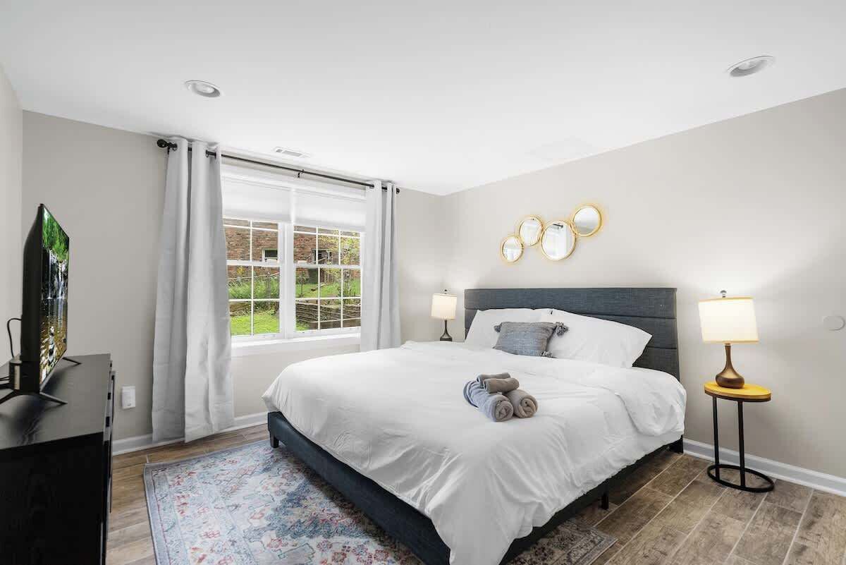 Een slaapkamer met een bed, een televisie, een raam met gordijnen en wandlampen.