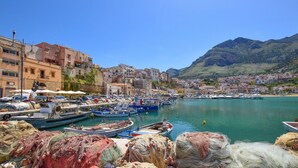 Una cittadina costiera con un porto turistico pieno di barche, edifici lungo il lungomare e montagne sullo sfondo.