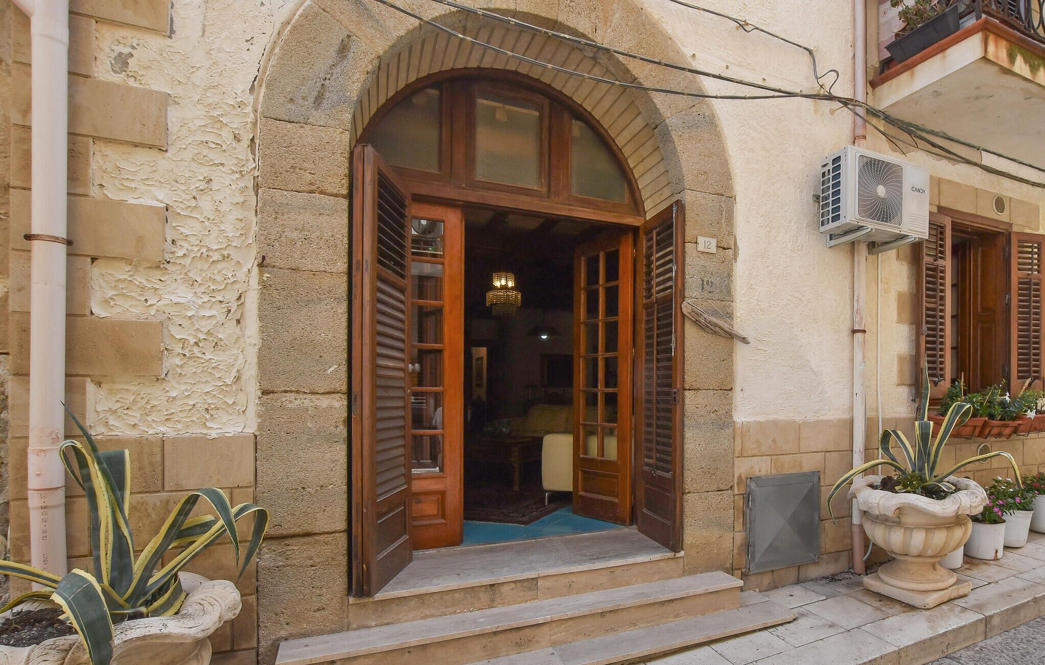 Ein Gebäude mit einer Fassade aus Stein, einer Holztür mit Glasscheiben und einem kleinen Vorbereich mit Topfpflanzen.