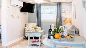 A cozy living room with a ceiling fan, a flat-screen TV, a sofa, a coffee table, and a dining table with chairs.