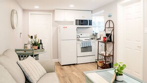 A compact living space with a kitchenette, a sofa, a small table, and a shelf with plants.