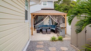 A covered patio area with a grill, seating, and a pergola.