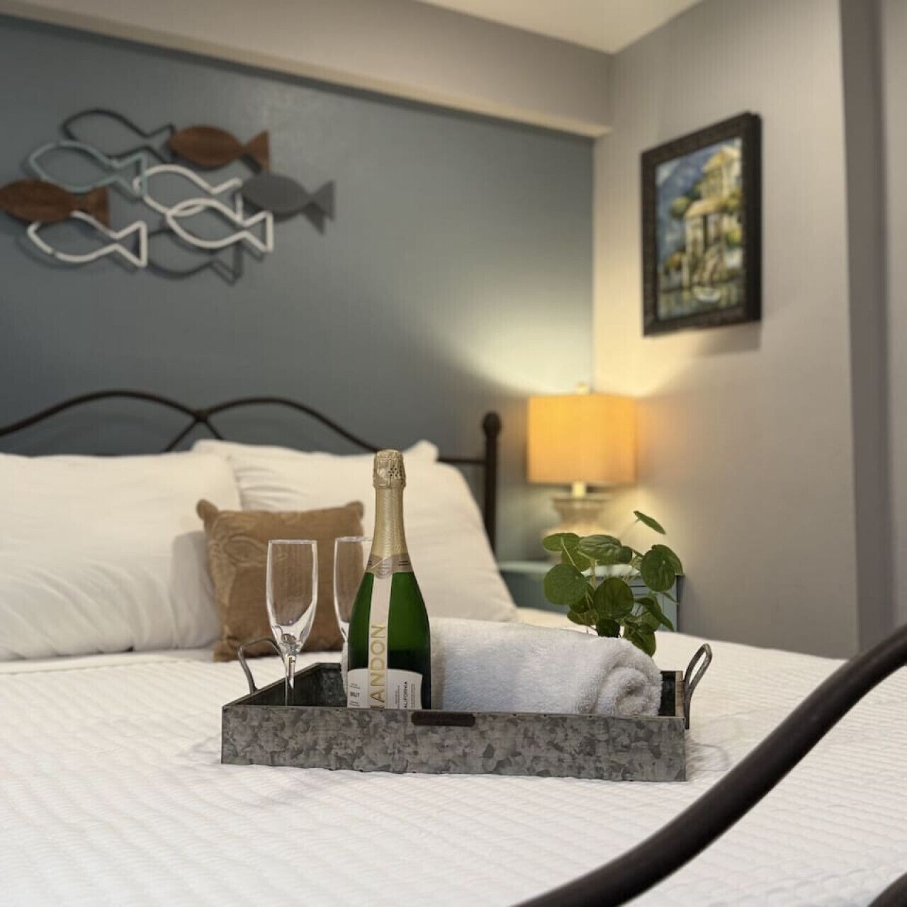 A neatly made bed with a tray holding a bottle of champagne, two glasses, and a folded towel.