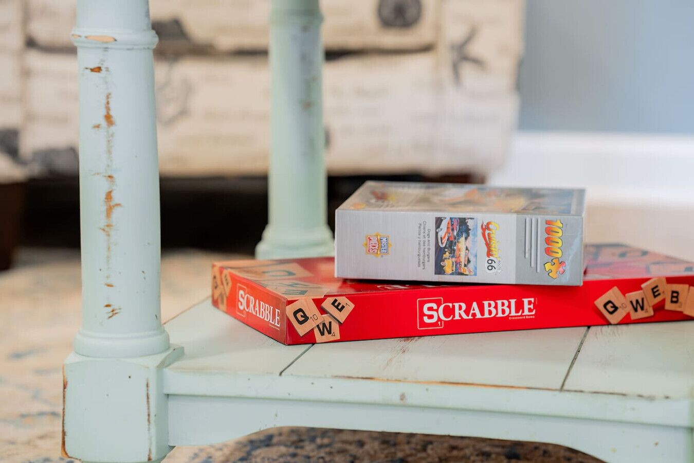 Une boîte de jeu de Scrabble posée sur une table en bois rustique, de couleur blanche.