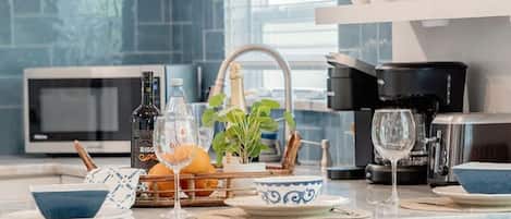 A modern kitchen with a central island, bar stools, a microwave, a coffee maker, and a window with blue-tiled walls.