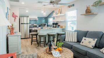 A modern living room with a grey sofa, a round wicker coffee table, and a kitchen in the background.