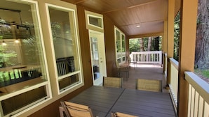 A covered porch with a table and chairs, large windows, and a view of the surrounding forest. - Fieldbrook Cottage in Redwood Forest (McKinleyville)
