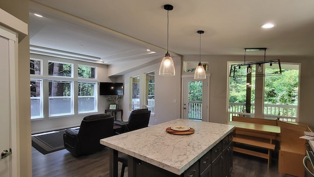 A spacious kitchen with a marble island, pendant lighting, and large windows offering views of greenery. - Fieldbrook Cottage in Redwood Forest (McKinleyville)
