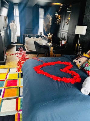 A bedroom with a bed, a desk, a chair, a bathtub, and a window.