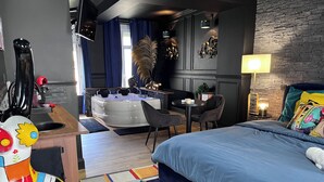 A modern hotel room with a large bed, a small desk, a seating area, and a bathroom. - La 104 private cocooning rooms with whirlpool bath (Saint-Omer)