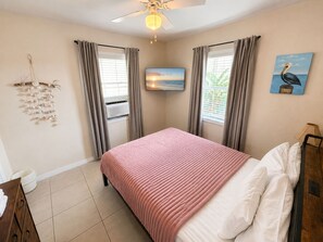 A bedroom with a bed, a ceiling fan, a TV, and a painting on the wall.