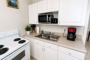 A kitchen with white cabinets, a stainless steel sink, a microwave, a stove, and a coffee maker.