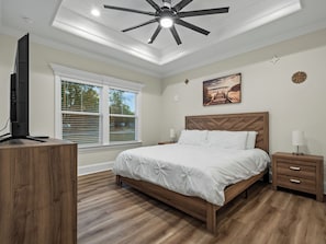Une chambre à coucher comprenant un lit, une table de chevet, un bureau, un ventilateur de plafond et une fenêtre avec des stores.