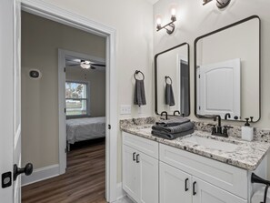 A modern bathroom with a large mirror, a sink with a faucet, and a toilet. There is a towel rack with towels and a door leading to a bedroom. - 4BR + near FSU/FAMU/Wakulla + firepit/BBQ on 1-acre (Crawfordville)