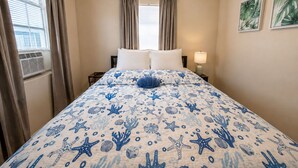 A hotel room with a bed, curtains, a window with blinds, a bedside lamp, and wall art. - Beachfront 1BR, Steps to Ocean, Dog Friendly. BOOK TODAY! (Redington Shores)