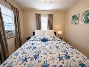 A hotel room with a bed, curtains, a window with blinds, a bedside lamp, and wall art. - Beachfront 1BR, Steps to Ocean, Dog Friendly. BOOK TODAY! (Redington Shores)
