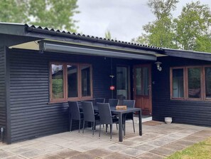 A modern black building with a covered patio area featuring a table and chairs. - 5 Star Holiday Home in Skagen (Aalbaek)