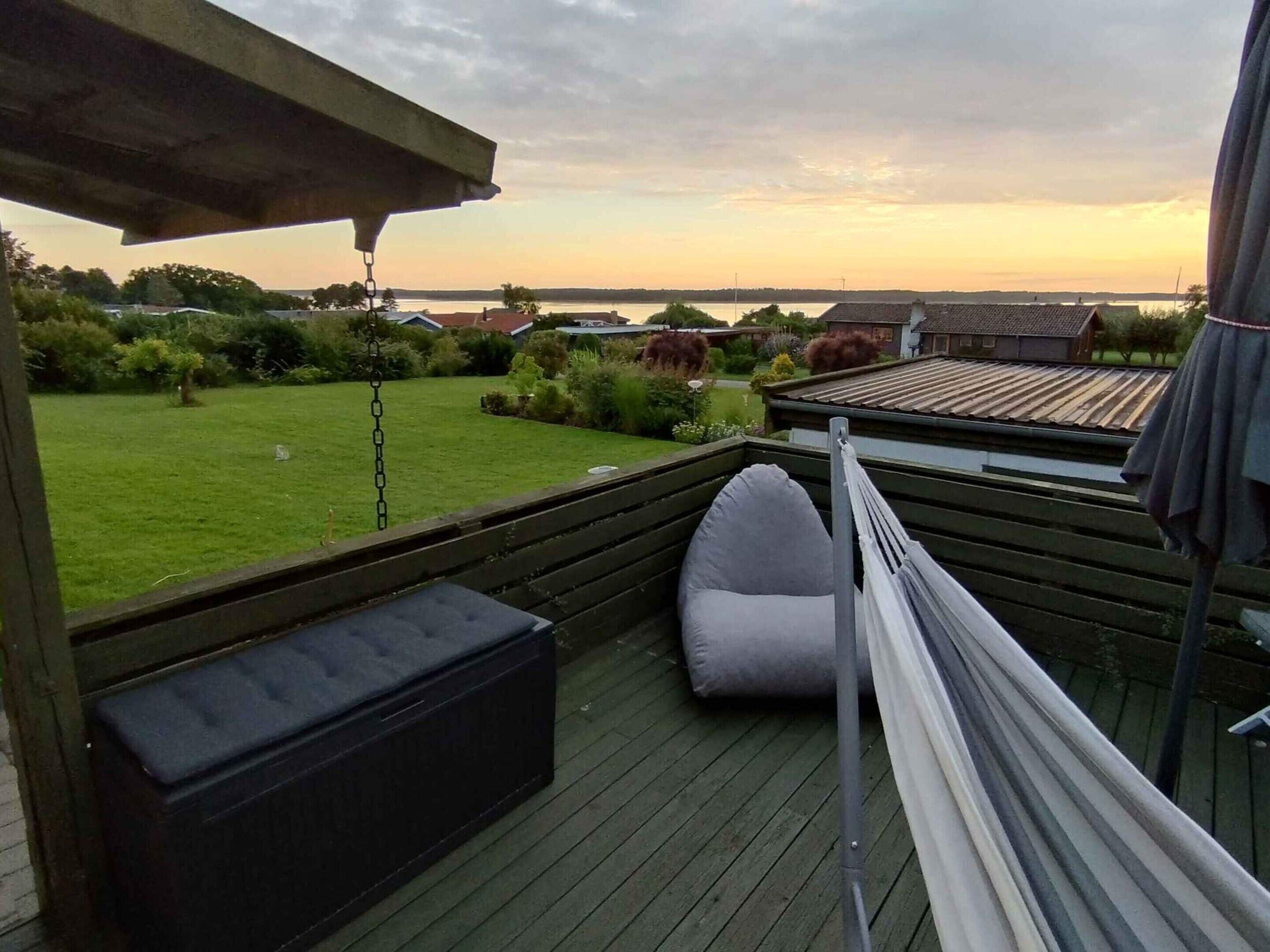 En terrasse med hængekøje, polstret bænk og udsigt over en græsplæne og huse i det fjerne.