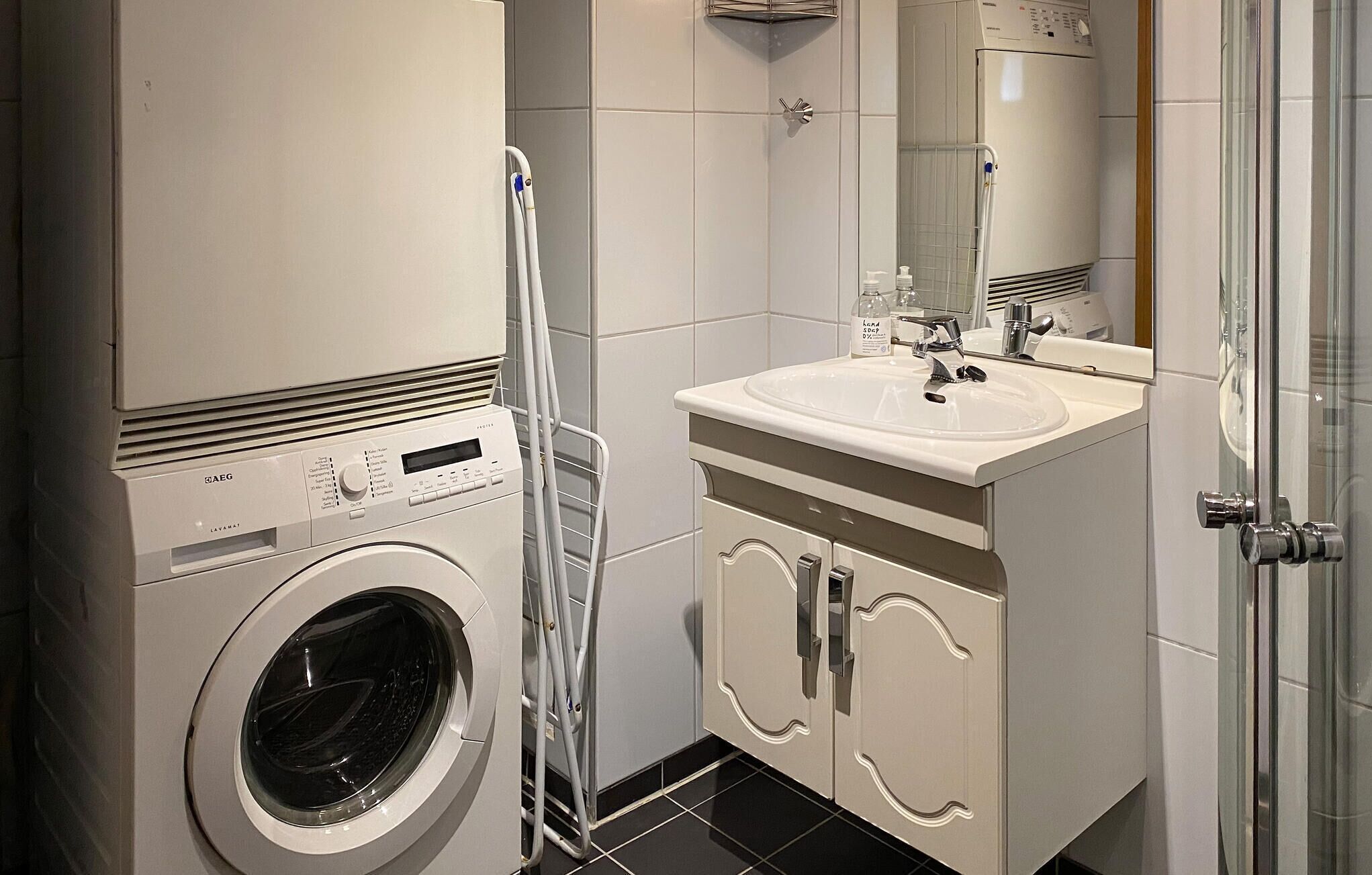 A compact bathroom with a washing machine, a sink, and a mirror.