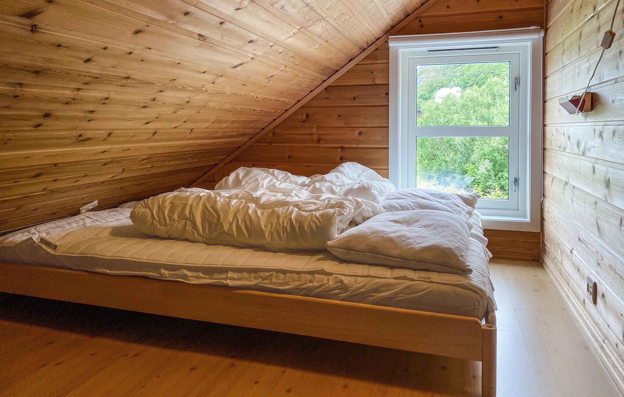 Un lit simple dans une pièce en bois avec un plafond en pente et une fenêtre.