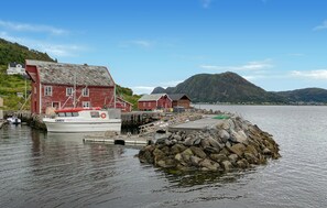 A coastal building with a dock, a boat, and a mountainous backdrop. - Gorgeous home in Leinøy with house sea view (Leinøy)