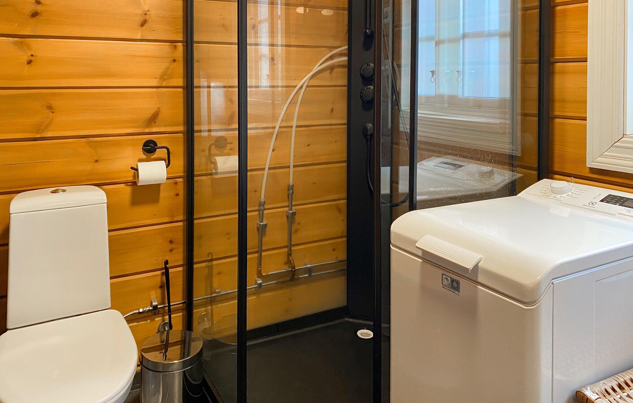 Une petite salle de bain comprenant des toilettes, un lave-linge et une cabine de douche en verre.