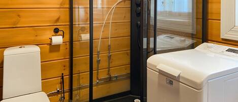 Une petite salle de bain comprenant des toilettes, un lave-linge et une cabine de douche en verre.
