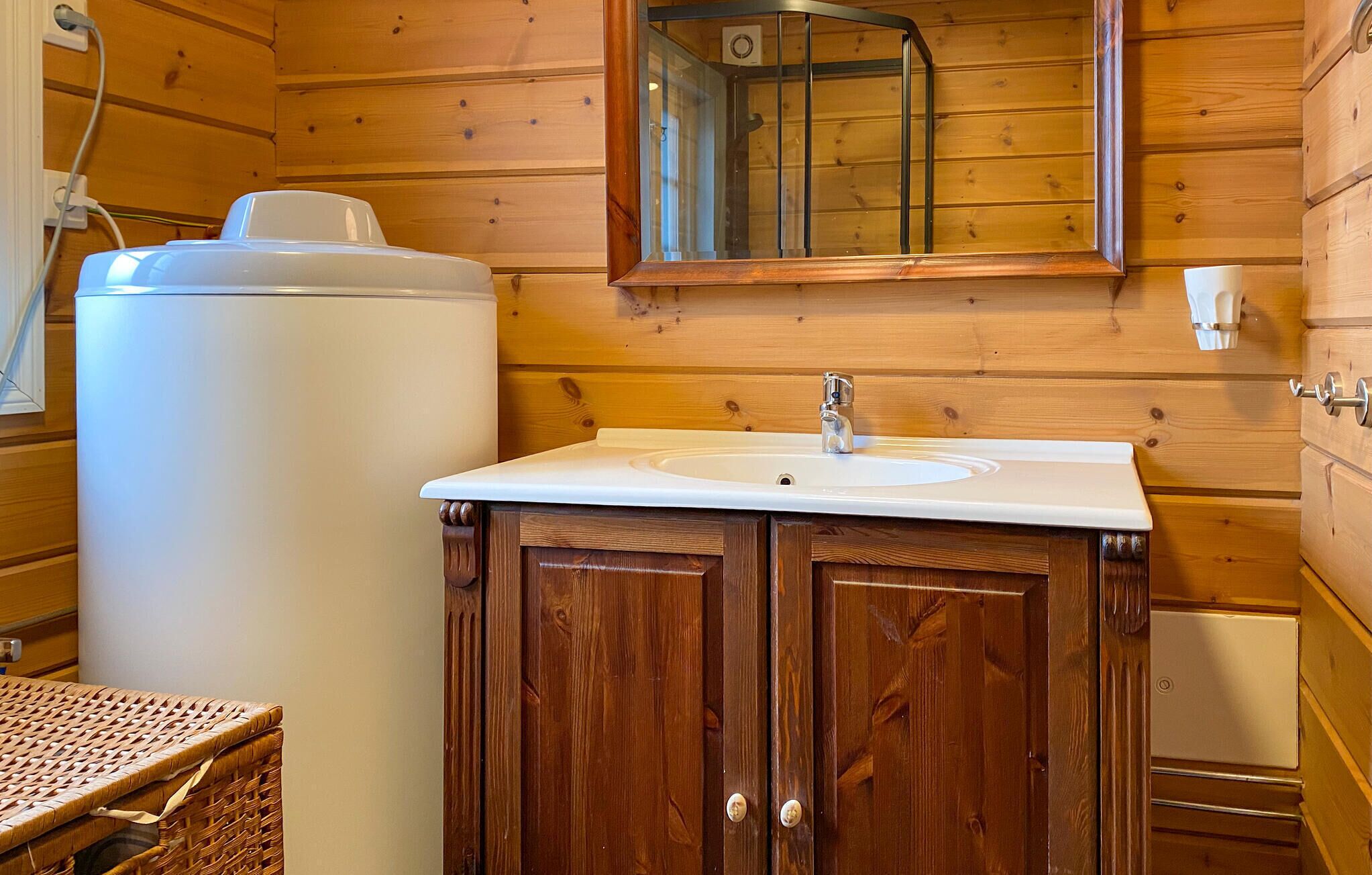 A wooden cabin bathroom with a white sink, wooden cabinets, and a white water heater.