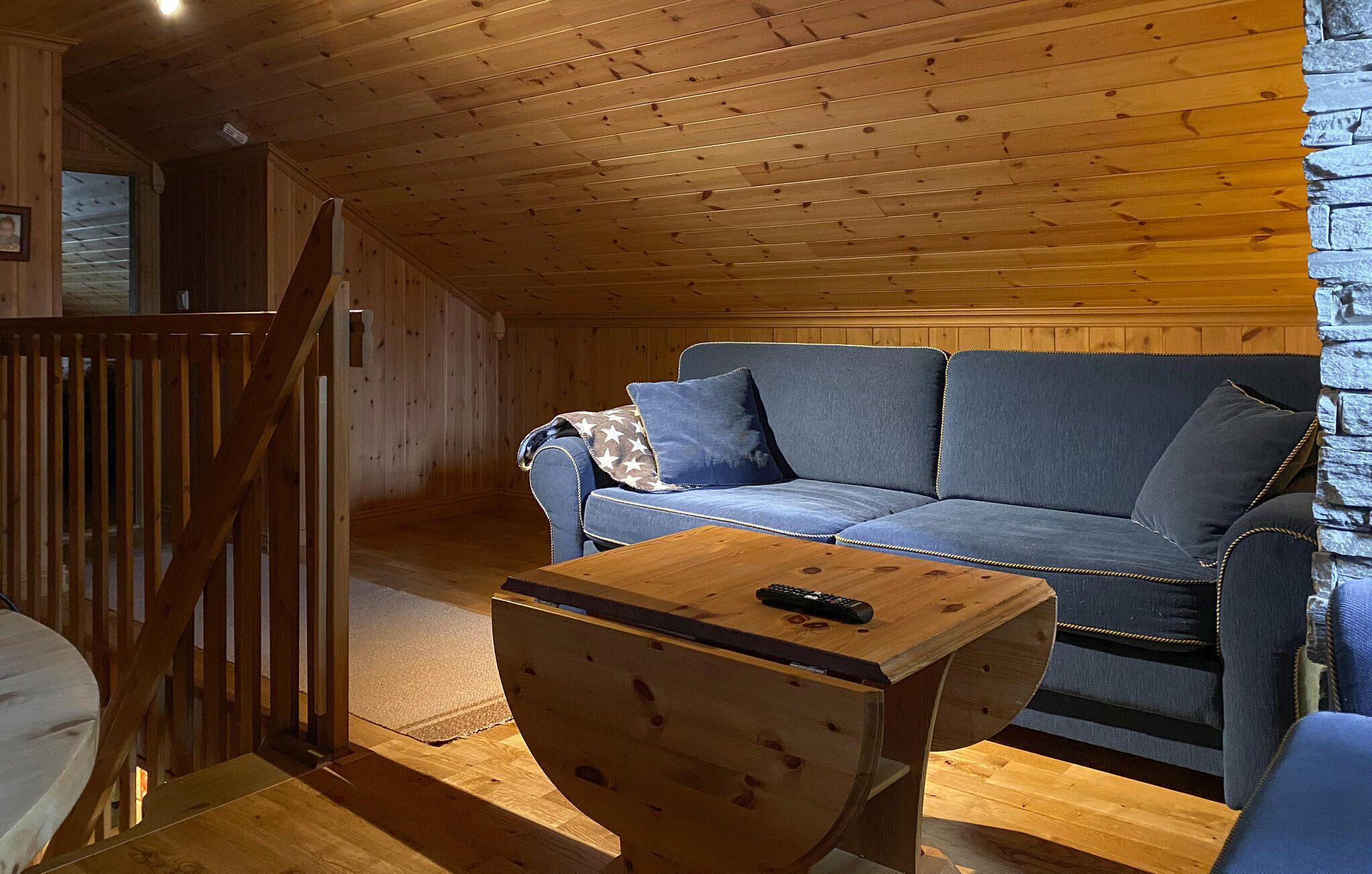 Een gezellig chaletinterieur met een houten plafond, een blauwe bank met kussens en een kleine houten tafel met een afstandsbediening.
