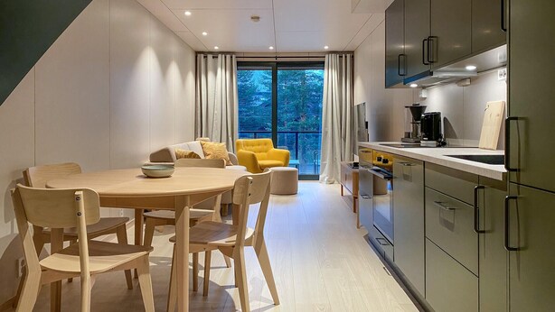 A modern kitchen with a dining area, featuring a large window with curtains, a yellow armchair, and wooden furniture. - Beautiful home in Bjorli (Bjorli)