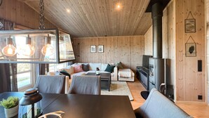 Ein gemütliches Blockhaus-Interieur mit Holzbalkendecke, einer Sofagarnitur, einem Tisch mit Laterne und einem Holzofen.