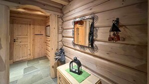 L’intérieur d’une cabane en rondins, avec une porte en bois, un miroir doté d’un cadre en métal, une petite commode en bois et une lanterne posée sur la commode.