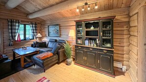 L’intérieur chaleureux d’un chalet avec un plafond en bois, un canapé, une table à manger et un buffet contenant de la verrerie.