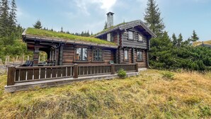 Une cabane rustique en rondins de bois, avec un toit végétalisé, une terrasse en bois et une cheminée.