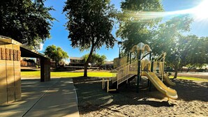 A playground with a slide and climbing structures, surrounded by trees and a paved area. - Civic Centre, Compact Microapt layout & Sprt Entry (Gilbert)