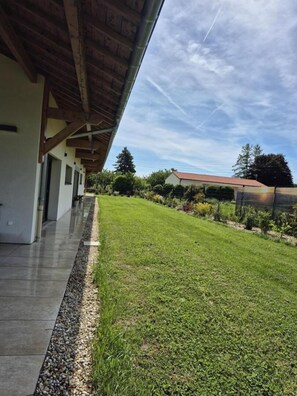 Uma área externa coberta com um caminho de pedras, um gramado e um prédio com telhado de telhas vermelhas ao fundo.