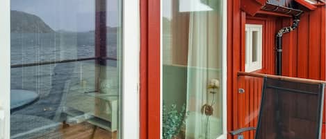 Ein Zimmer mit einer großen Glasdoor, die auf einen Balkon mit Blick auf das Meer und die Hügel führt.